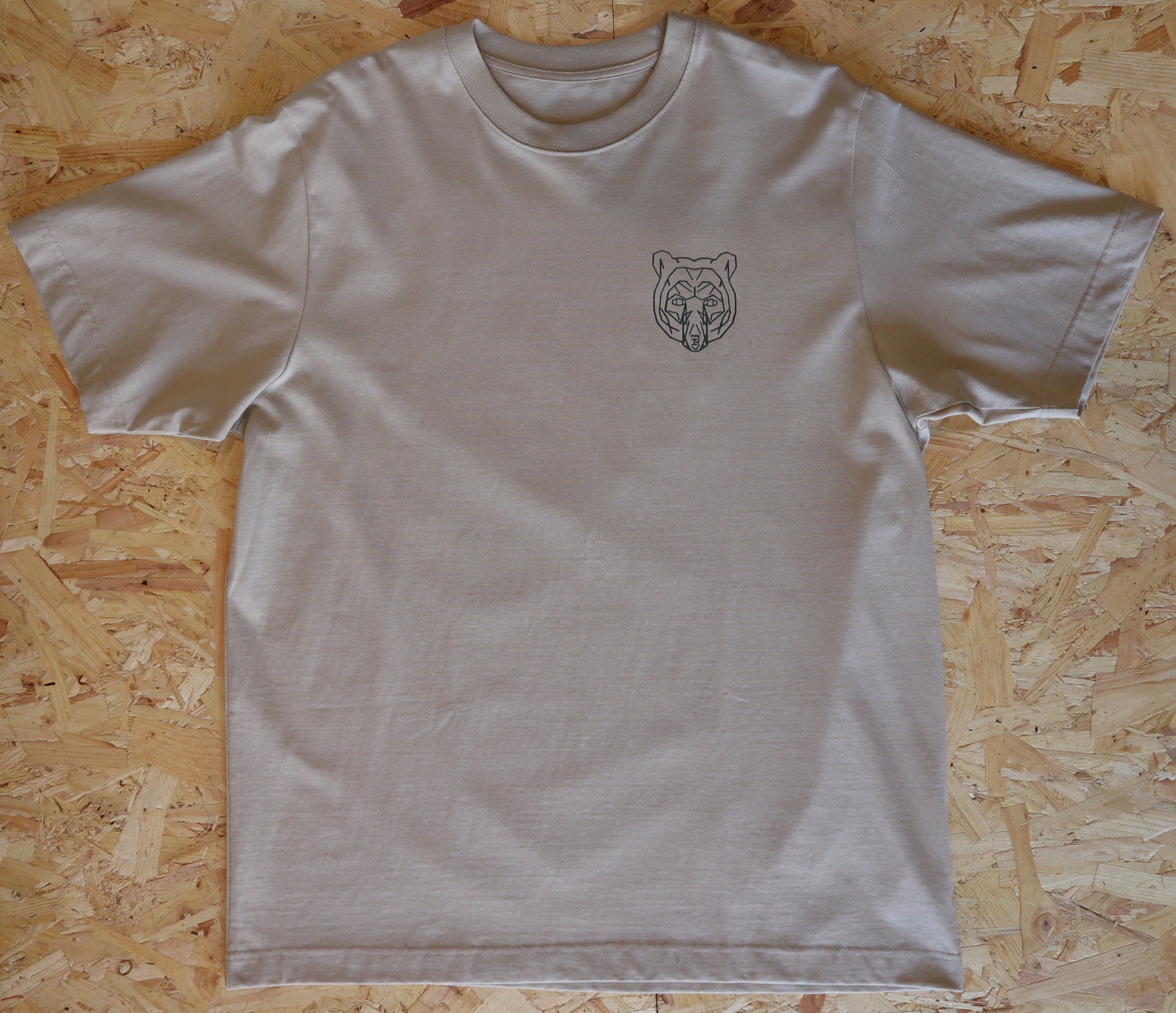 Beige t-shirt with a bear logo on a wooden surface