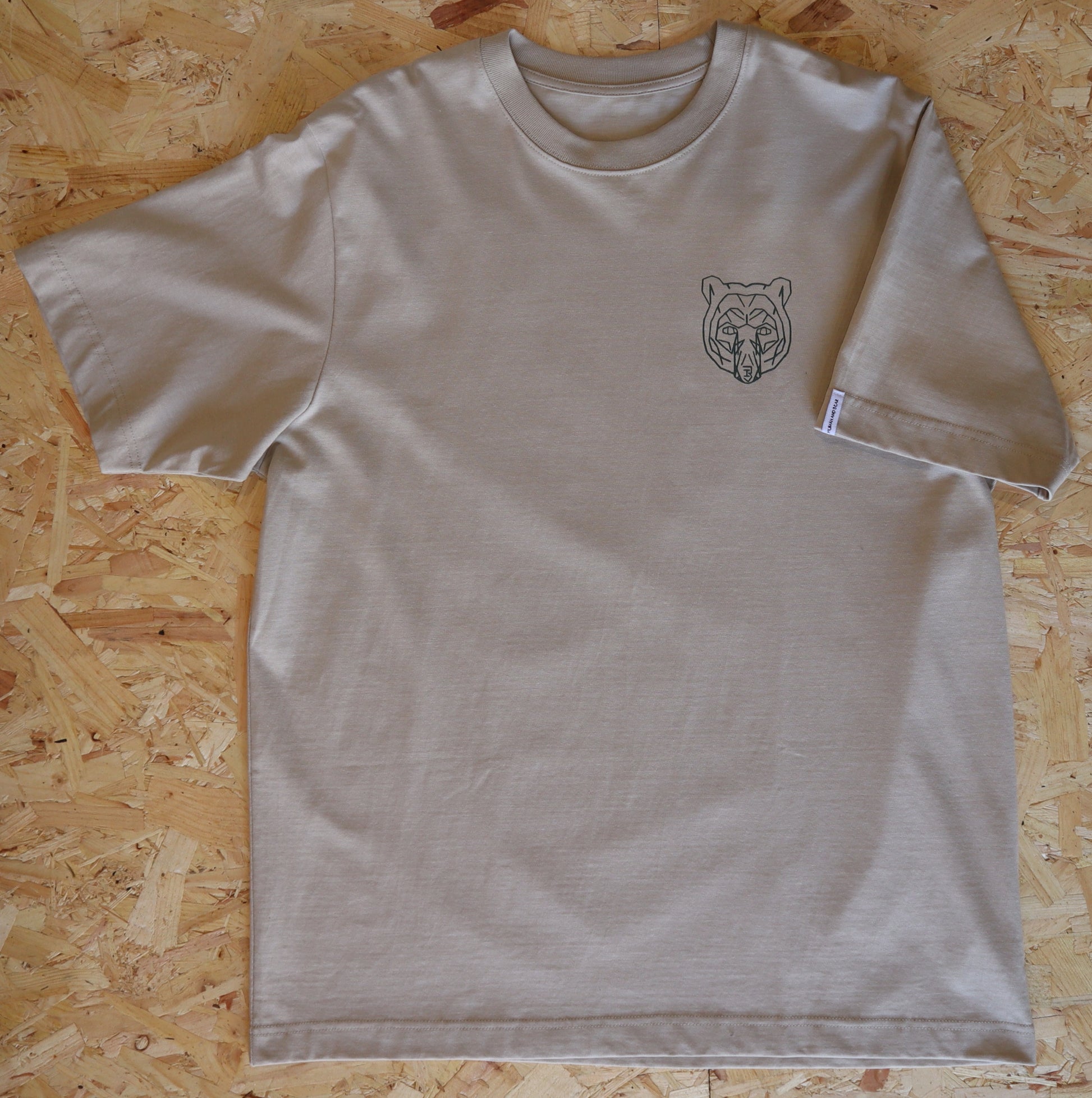 Beige t-shirt with a bear logo on a wooden surface