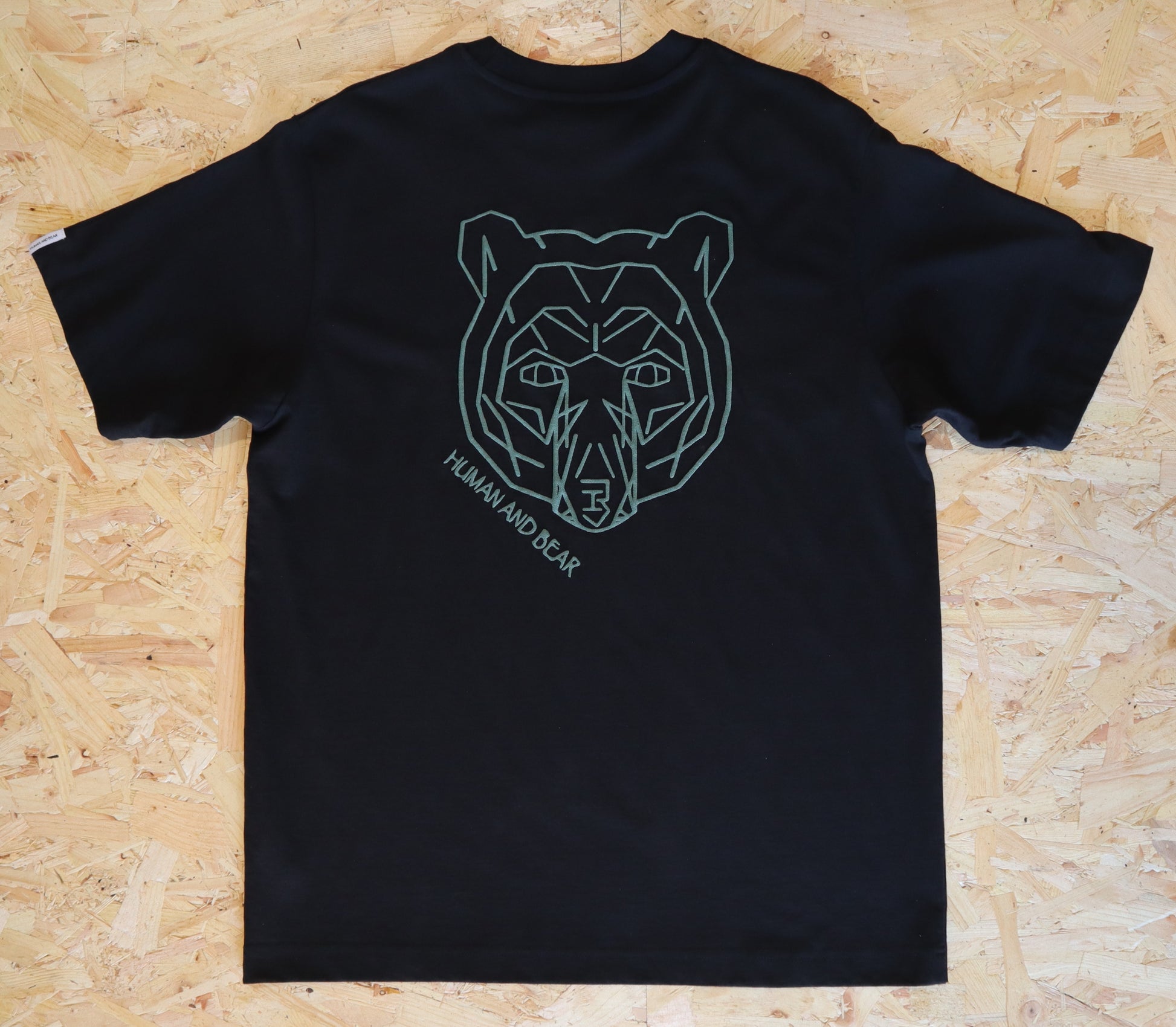 Black t-shirt with a bear graphic and Human and bear text on a wooden surface