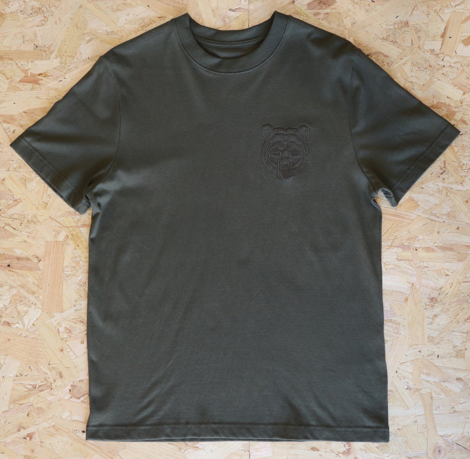 Khaki t-shirt with a bear logo on a wooden surface