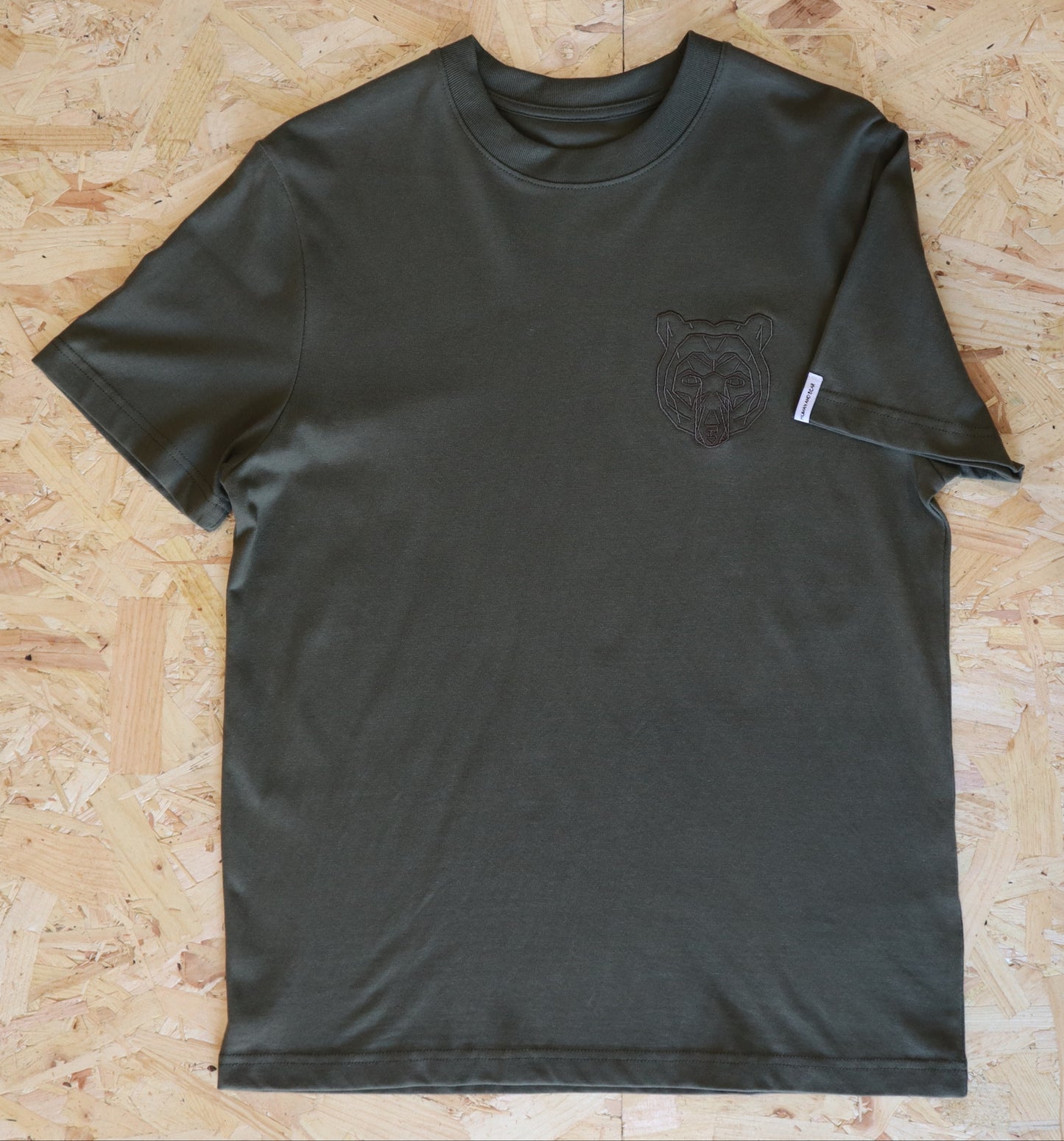 Khaki t-shirt with a bear logo on a wooden surface