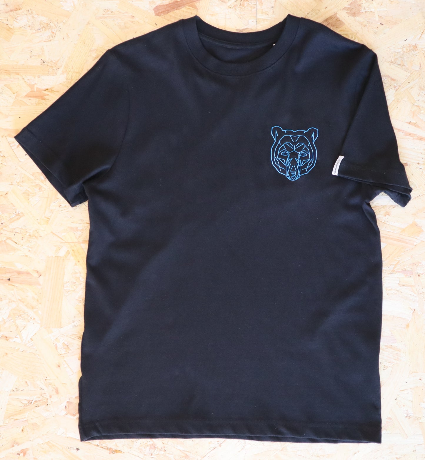 Black t-shirt with a blue bear logo on a wooden surface