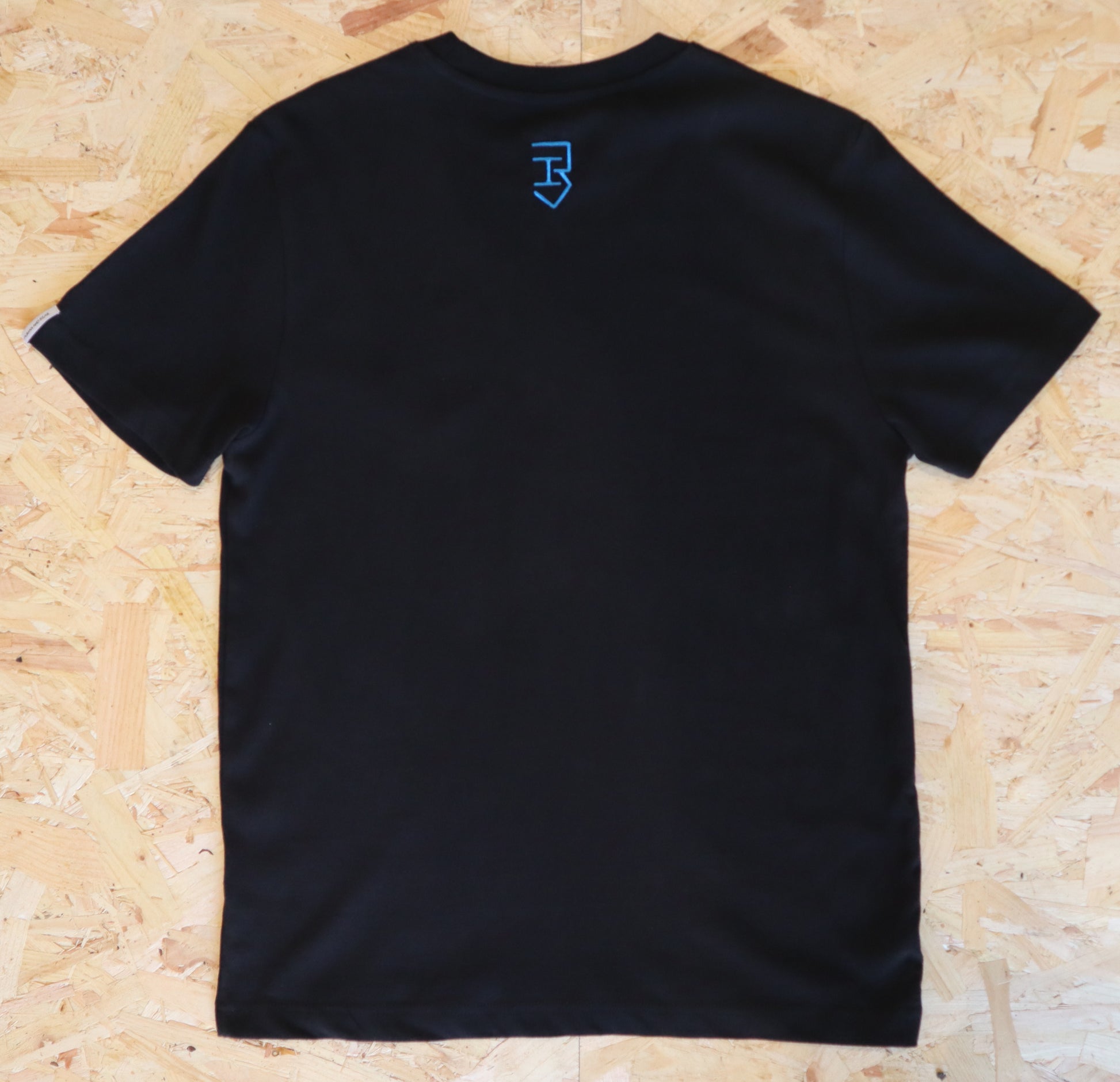 Black t-shirt with a blue logo on the back, on a wooden surface.