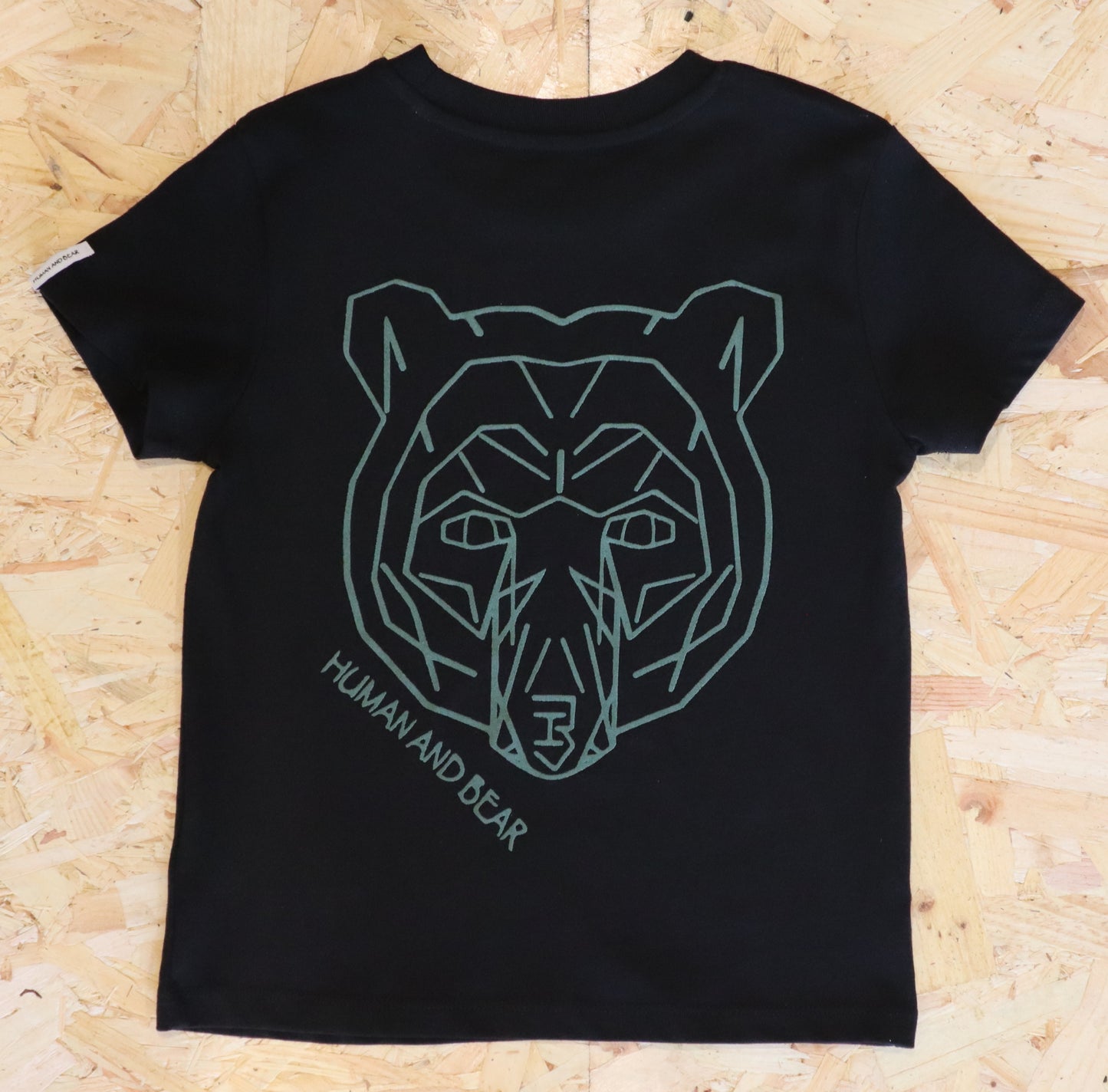 Black t-shirt with green geometric bear design on a wooden surface