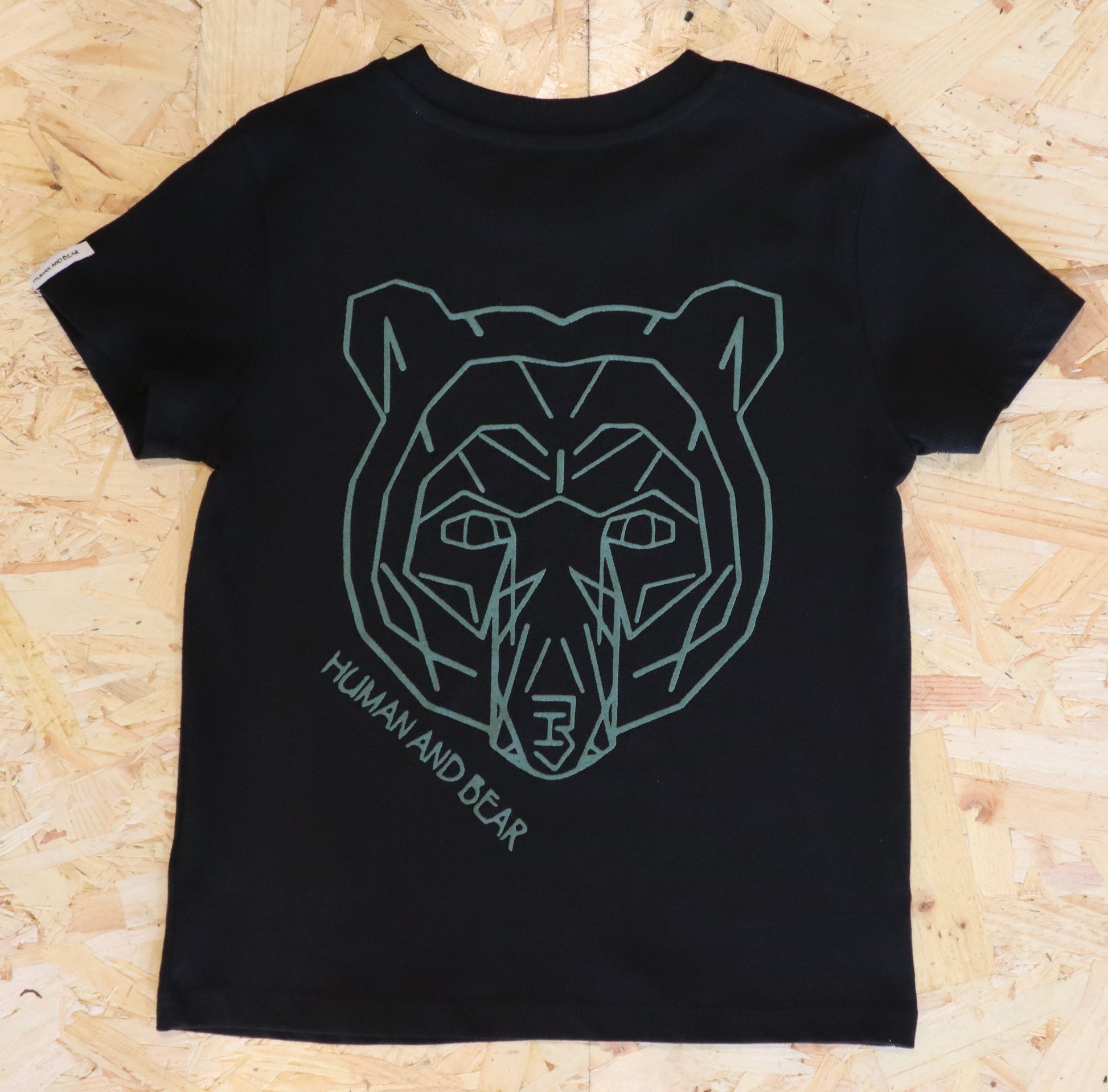 Black t-shirt with green geometric bear design on a wooden surface