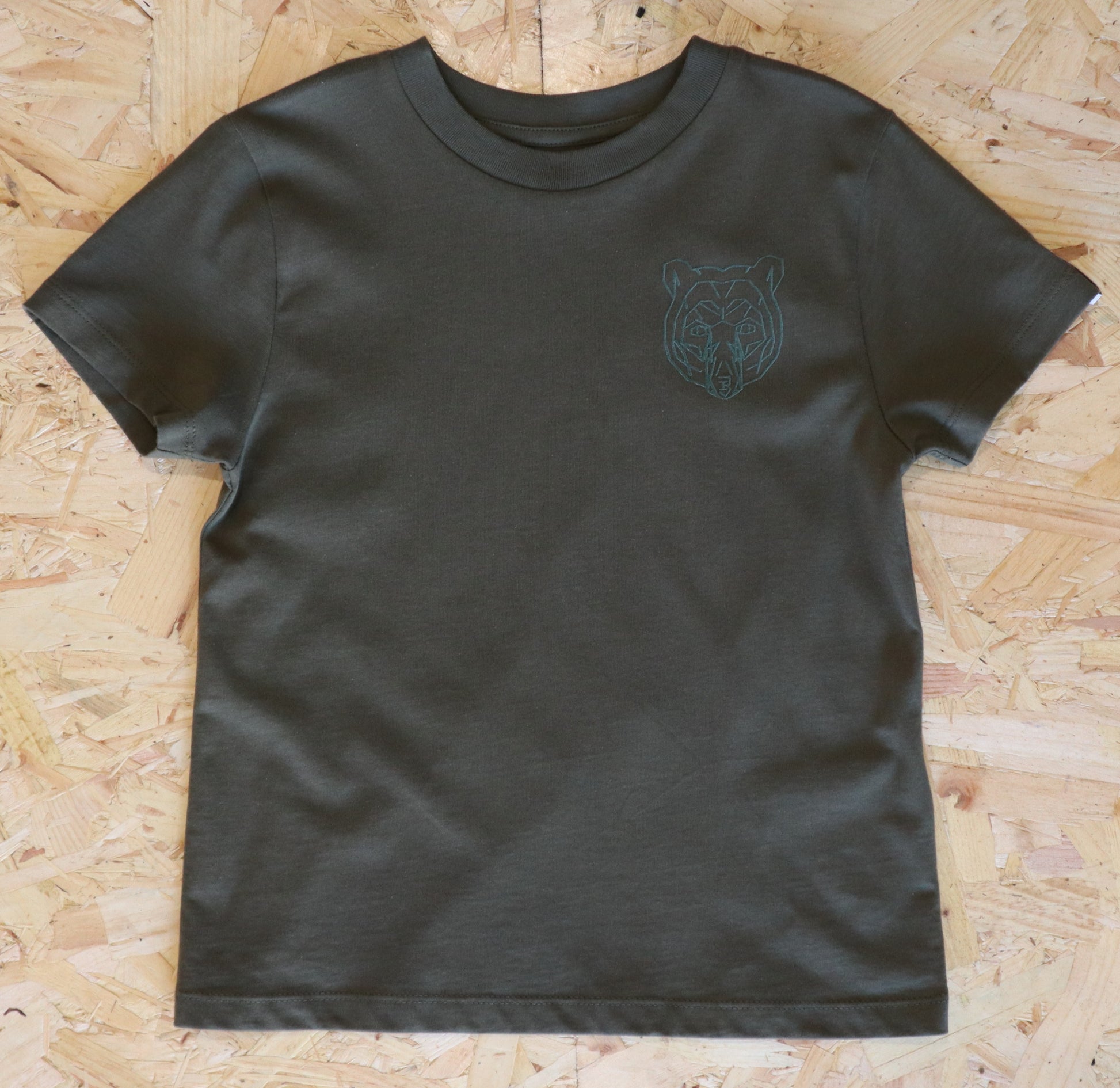 Khaki  t-shirt with a green bear logo on a wooden surface