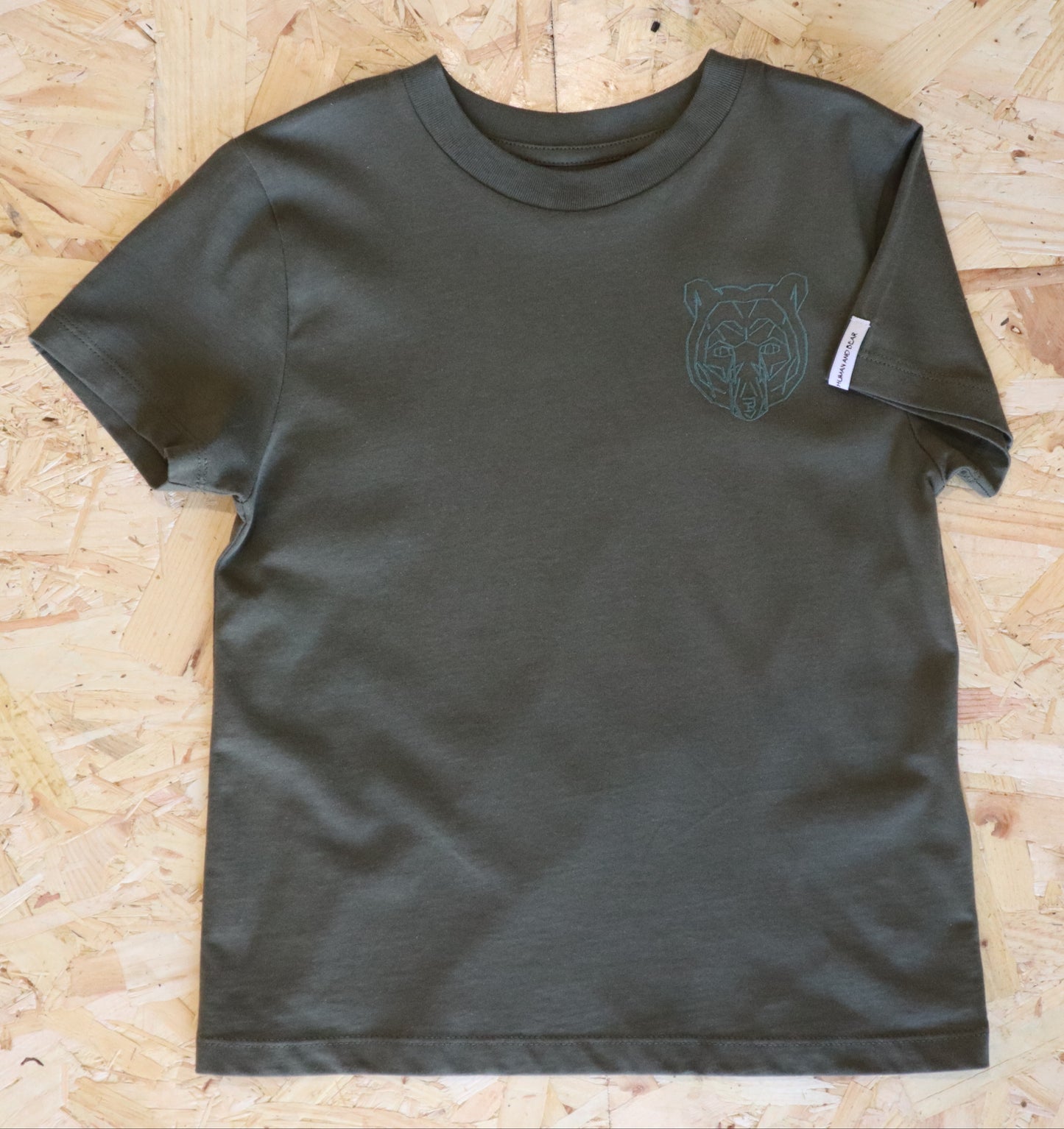 Khaki t-shirt with a bear graphic on a wooden surface