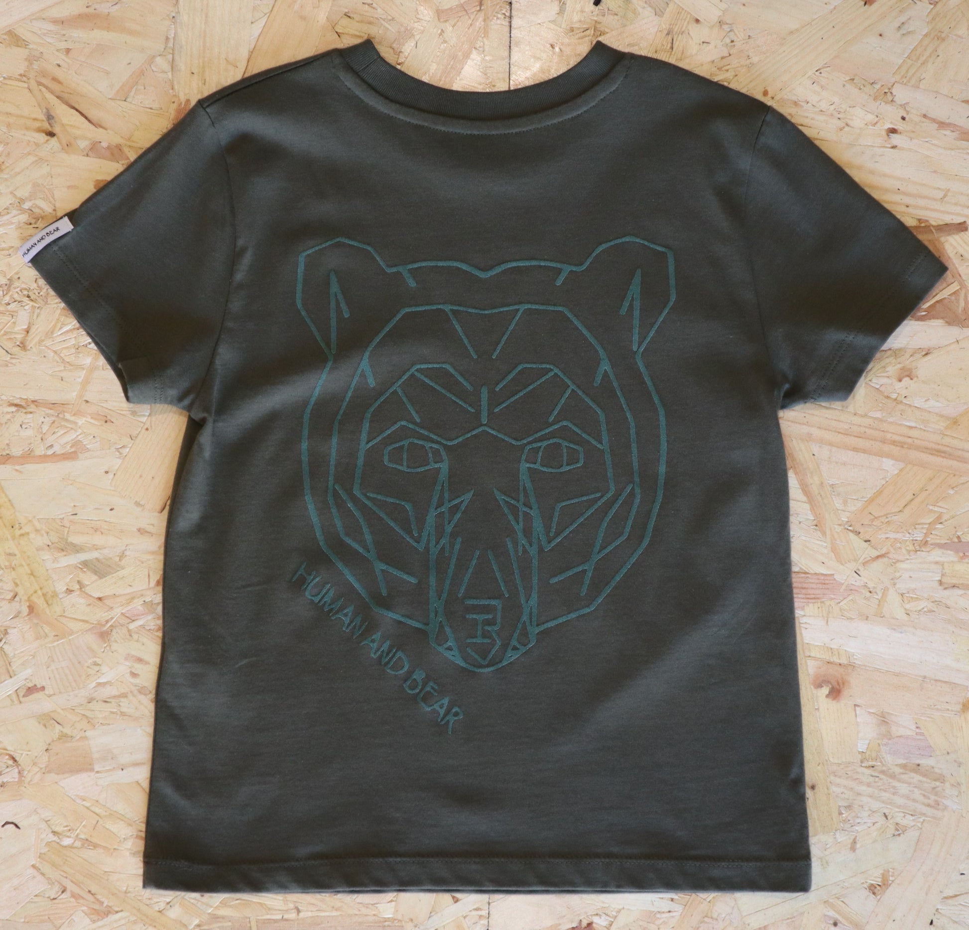 Khaki t-shirt with a bear graphic on a wooden surface